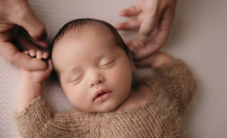 newborn baby lying on back holding parents hands during a newborn photoshoot