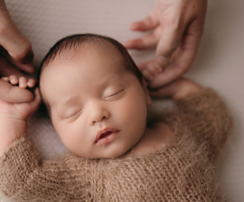 newborn baby lying on back holding parents hands during a newborn photoshoot