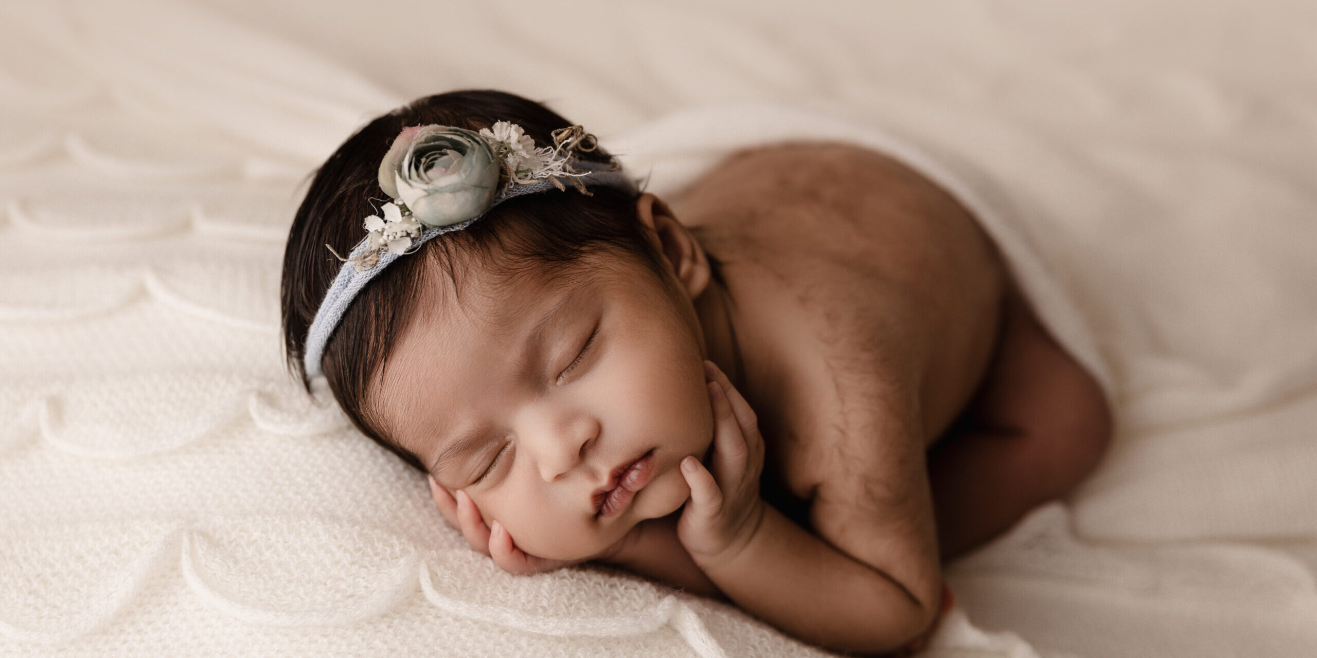 picture of newborn baby wearing a blue floral headband and laying on a white ruffle backdrop during a newborn photoshoot