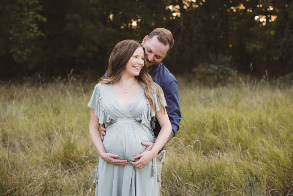 couple in a field holding a pregnant tummy during their maternity photo session